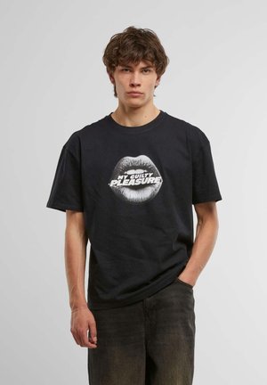Sort bomulds T-shirt med et stort hvidt grafik af læberne og teksten "MIT SKYLDIGE NEDERLAG" centreret nedenfor. Løs pasform og korte ærmer.
