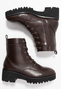 Bottes chelsea en cuir synthétique marron avec laçage sur le devant, fermeture éclair latérale, bout arrondi, et semelle en caoutchouc noir texturée avec crampons profonds.