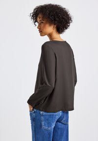 Donker, effen blouse met lange mouwen, gladde textuur en een ronde hals, gecombineerd met blauwe spijkerbroek. Eenvoudig ontwerp, geen patronen.