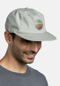 Gorra gris clara de algodón con visera plana y logo bordado "Solo Buenas Vibras" en multicolor, con un diseño redondo.