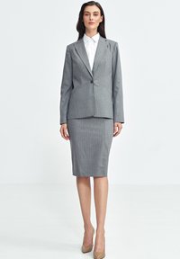 Szary garnitur w prążki z dopasowaną marynarką i spódnicą do kolan, sparowany z białą koszulą z kołnierzykiem. Gładki materiał z dopasowanym krojem.