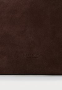 Hnědá semišová tkanina s hladkým povrchem, se zlatě embosovaným logem "Marc O'Polo" a nápisem "Založeno ve Stockholmu" ve spodní části.