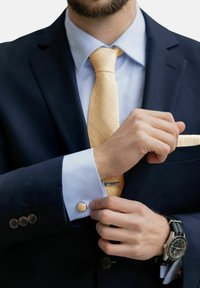 Abito navy con camicia azzurro chiaro e cravatta a motivi di diamante gialla. Presenta gemelli d'argento e un orologio nero con dettagli argentati.