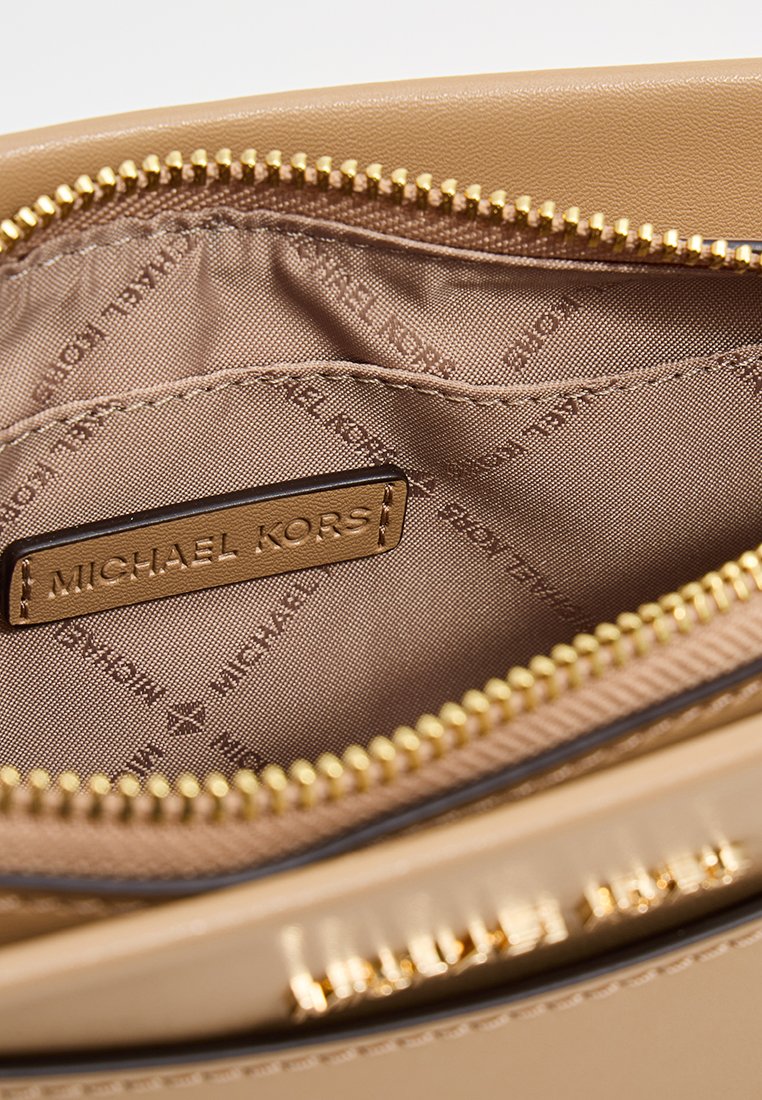 Binnenkant van een tan leren tas met een gouden ritssluiting. Voering heeft een herhalend "MICHAEL KORS" patroon. Gladde textuur, schoon ontwerp.