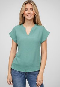 Tyrkise topp med en avslappet passform, korte ermer og V-hals design. Teksturlig stoff, kombinert med blå jeans.