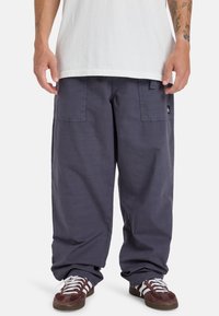 Loszittende marineblauwe cargobroek met twee voorzakken, gemaakt van duurzaam materiaal. Voorzien van een subtiel merkembleem aan de zijkant.