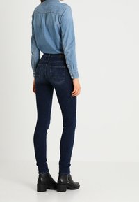 Ljusblå denimskjorta med knappar, i kombination med mörkblå skinny jeans och svarta ankelskor med tjock klack.