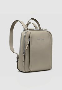 Mochila beige claro con textura suave, con correas ajustables, cremalleras dobles y un logotipo sutil en el frente.