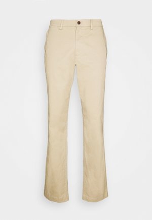 Pantalones de campana beige hechos de algodón, con cierre de botón frontal, presillas para cinturón y una textura suave. Corte entallado con piernas rectas.