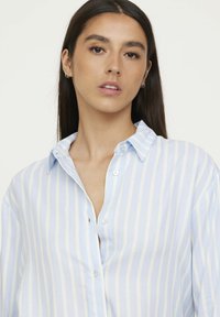 Light blue and white striped button-up shirt featuring a collar, relaxed fit, and smooth fabric with a slight sheen. Buttons are white.