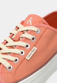 Calvin Klein tenisice u koraljnoj platnu s bijelim vezicama, okruglim vrhom, metalnim rupama za vezanje i detaljem logotipa na jeziku i strani. Bijela potplata.