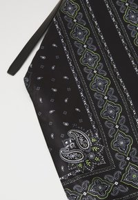 Melns auduma soma ar zaļiem un baltajiem paisley un ziedu rakstiem, melna siksna un maziem baltajiem asaras un kvadrāta formas elementiem.