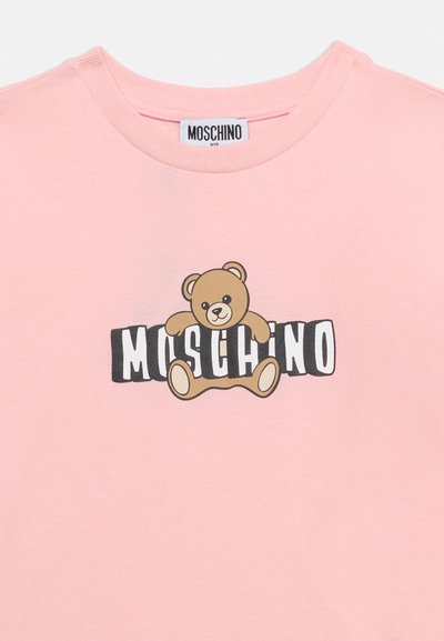 Ροζ βαμβακερό μπλουζάκι με γραφικό καφέ αρκουδάκι και μαύρα γράμματα που σχηματίζουν τη λέξη «MOSCHINO» από κάτω. Κλασικός στρογγυλός λαιμός και κοντά μανίκια.