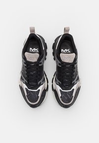 Des chaussures de sport noires et grises avec des surfaces texturées, un design à lacets, un logo sur la languette et des semelles en caoutchouc épaisses. Elles disposent d'une languette de traction au talon.