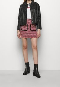 Veste en cuir noire avec des accents cloutés, t-shirt blanc avec texte rose, mini-jupe à motif pied-de-poule rose et noir, et bottines à talons noires.