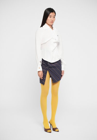 Witte lange mouwen shirt met een gestructureerde voorkant, gecombineerd met een donker gestreepte mini rok met een geknoopte detail, gele maillot en open teen hakken.