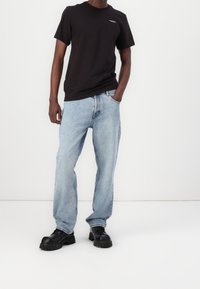 Zwarte katoenen T-shirt met ronde hals en logo, gecombineerd met lichtblauwe denim jeans met een relaxte pasvorm en chunky zwarte schoenen met een dikke zool.