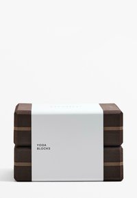 Hnedé jogové bloky poskladané na sebe, zabalené v bielom páse. Text na páse znie "Jogové bloky." Hladký povrch a obdĺžnikový tvar.