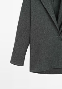 Ciemnoszary żakiet wykonany z teksturowanej tkaniny, z wyłamiwanym kołnierzem, pojedynczym zapięciem na guzik oraz długimi rękawami z prostym dołem.