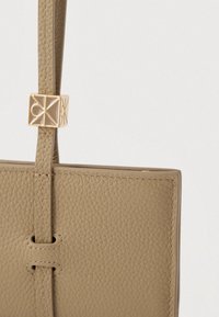 Χειροποίητη τσάντα ώμου από χακί δέρμα με υφή, που διαθέτει κομψό σχήμα, εξαρτήματα σε χρυσούς τόνους και ρυθμιζόμενο λουράκι για ευελιξία.