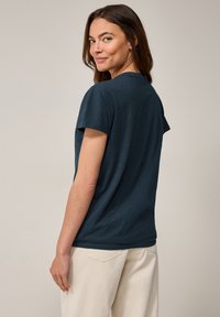 T-shirt corto a maniche corte di colore blu scuro in una vestibilità rilassata, con scollo rotondo e una texture morbida. Indossato con pantaloni chiari.