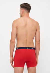 Boxeri roșii cu talie albastră închisă, având inscripția "GAP", realizați dintr-un material moale și elastic, care pune accent pe un design ajustat.