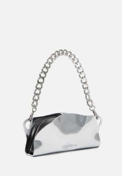 Metallic silver handbag with a chain strap, featuring a sleek, curved design, and a black zippered compartment. Text "PUBLISHED BY" visible.
