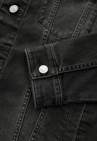 Schwarze Denimjacke im Close-up, mit einem geknöpften Bündchen, sichtbaren Nähten und einer weichen Textur. Es sind keine bemerkenswerten Muster oder Akzente vorhanden.