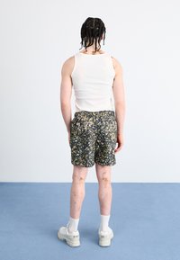 Black floral shorts with yellow and pink accents, paired with a white tank top. Features a classic fit and elastic waistband. White sneakers.