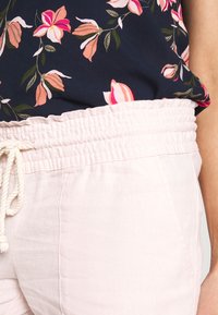 Pantaloni in misto lino rosa chiaro con vita elasticizzata e cordino. Abbinati a una maglietta blu scuro con motivi floreali rosa e bianchi.