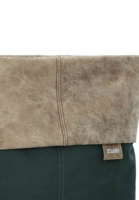 Bruine faux lederen top met een gestructureerde afwerking en een groene stoffen body. Zijkant label zichtbaar. Gestikte details langs de naad.