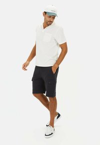 Hvid kortærmet polo skjorte med en forlommel, parret med marineblå cargo shorts med sidelommer, båret med hvide sneakers.