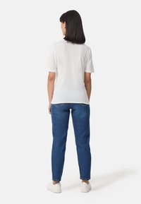 Witte t-shirt met korte mouwen, van zacht katoenen stof, met een ronde halslijn. Gecombineerd met blauwe spijkerbroek, slim fit, met opgerolde zoom en witte sneakers.