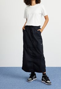 Svart, ankellång kjol med elastiskt midjeband och fickor, i kombination med en vit t-shirt och svarta högstövelskor.