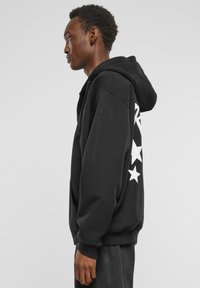 Black hoodie made of soft fabric, featuring a large white star graphic along the left side, with a drawstring hood and ribbed cuffs.