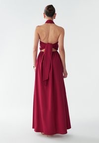 Vestido largo burdeos con cuello halter y espalda descubierta. Presenta un lazo atado en la cintura y una falda fluida, confeccionado con una tela suave.