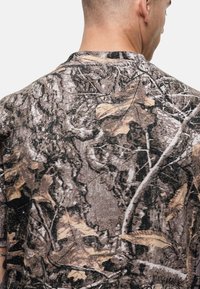 Camo short-sleeve shirt in brown and gray with leaf and bark patterns; soft texture; crew neck; fabric drapes smoothly on the shoulders.