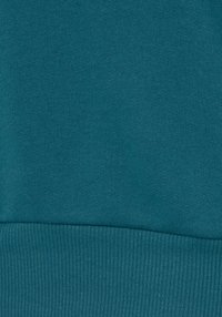 Teal värviga kapuutsiga särk, millel on sile tekstuur; alumisel serval on soonikkoes äär, mis loob peene kontrasti tekstuuri ja viimistluse vahel.