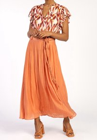Top avvolgente a fantasia floreale con maniche a volant, abbinato a una lunga gonna arancione fluida con dettaglio di legatura intrecciata e sandali con tacco a blocco.