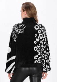 Pulover fuzzy alb-negru cu modele îndrăznețe, inclusiv printuri circulare și leopard, cu guler înalt și mâneci largi.
