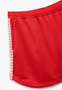 Rode shorts van een gladde stof, met een witte kantafwerking langs de zijkant. De tailleband is elastisch voor een veilige pasvorm.