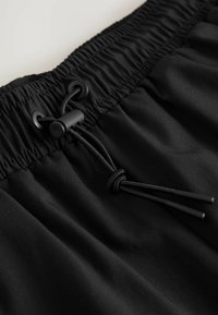 Sorte shorts med et elastisk taljeled og snøre. Lavet af glat, let stof. Har en indsnævret talje og en subtil glans.