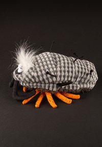 Plush toy resembling a bug with a gray checkered body, orange legs, and black accents. Features fuzzy white hair and black antennae.