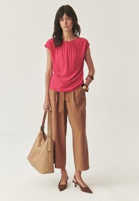 Fuchsia bluse med rynket halsudskæring, parret med beige vidde bukser. Brune spidse hæle og en stor beige skuldertaske.