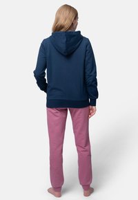 Felpa con cappuccio blu navy, maniche lunghe e polsini a costine, abbinata a un paio di pantaloni della tuta rosa, vista dal retro. Texture del tessuto liscia.
