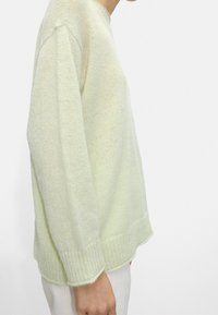 Pull vert clair en maille avec une coupe décontractée, présentant un ourlet côtelé, des épaules tombantes et un tissage texturé.