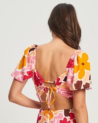 Top corto a stampa floreale con maniche a sbuffo corte, scollatura bassa con dettaglio a lacci e colori vivaci tra cui rosa, arancione e marrone.