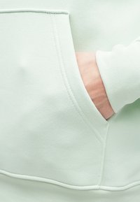 Φούτερ σε μέντα πράσινο με τσέπη καγκουρό και ριμπ μανσέτες. Απαλή, υφασμάτινη υφή με ορατές ραφές λεπτομερειών.