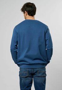 Felpa di cotone blu con collo a girocollo a coste e maniche lunghe, indossata con jeans di denim blu. Design semplice, tinta unita, senza motivi.