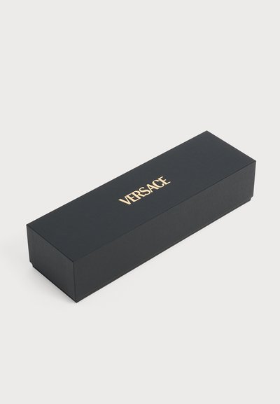 Boîte rectangulaire noire avec logo VERSACE doré centré en haut, posée sur une surface grise claire unie.